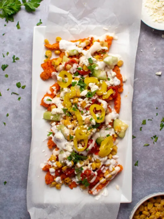 Mediterranean street fries with feta cheese, banana peppers, and corn on parchment paper lined platter.
