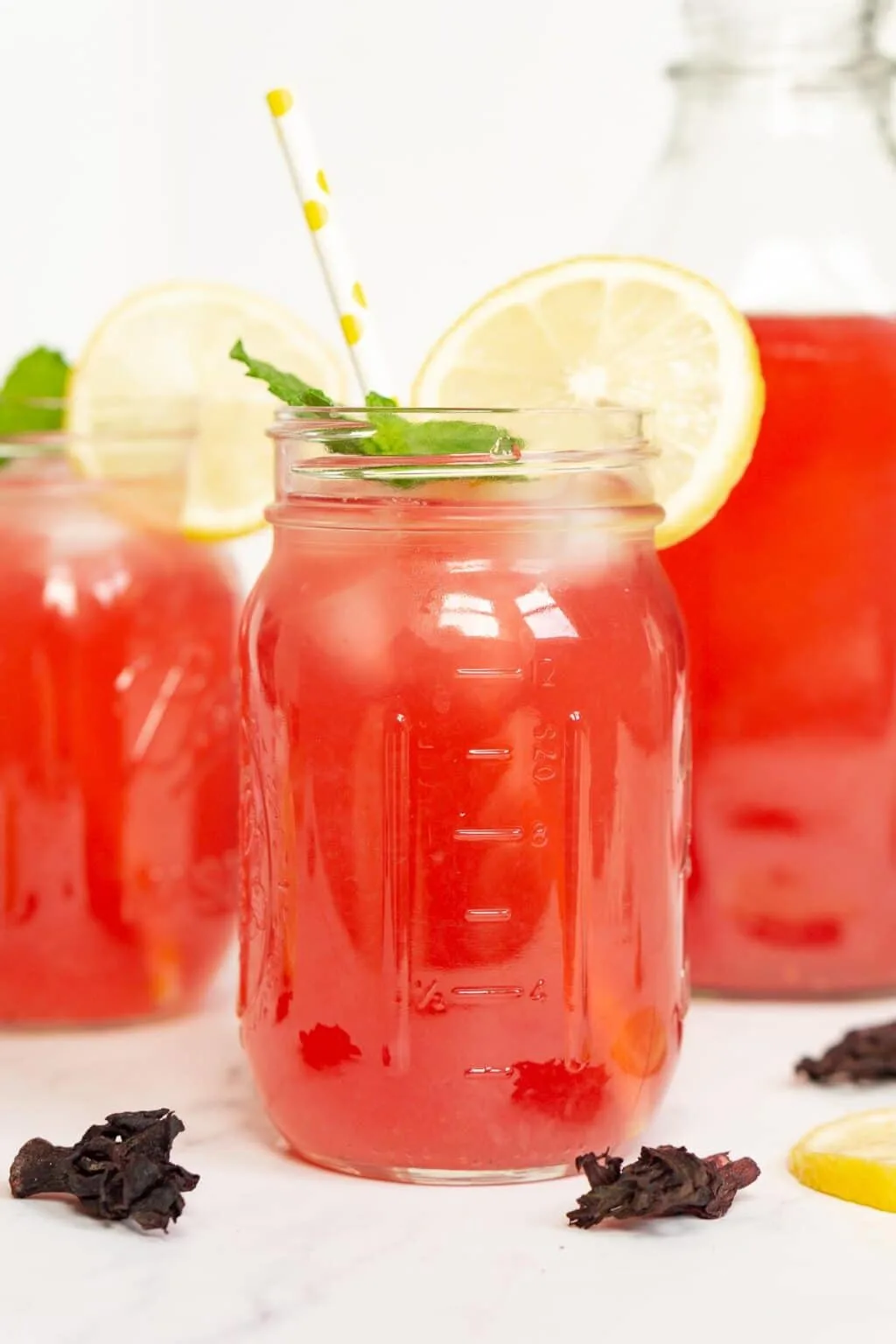 Hibiscus tea lemonade in mason jars with white and yellow straws and lemon mint garnish.