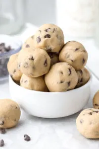 No-bake cookie dough bites piled in a white bowl with chocolate chips.