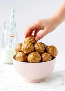 Large stack of oatmeal peanut butter balls in a pink bowl with a glass of milk.