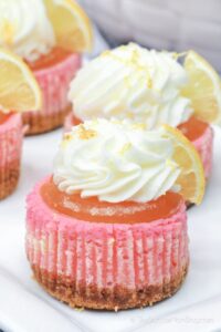 Pink lemonade cheesecakes with white frosting and lemon garnish.