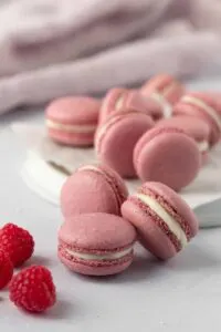 Raspberry macaroons stacked on each other with fresh raspberries in foreground.