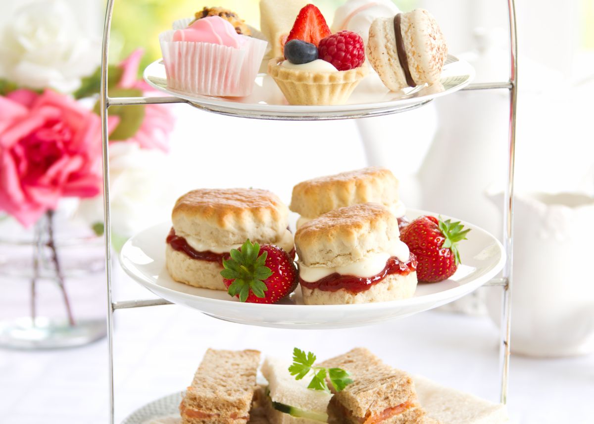 Tiered tray filled with tea party sandwiches and sweets on a white table.