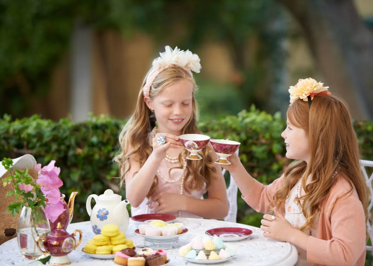 Two girls clink their tea cups and an outdoor tea party.