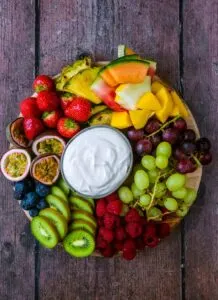 Fruit platter with several types of fresh fruit and a bowl of creamy dip in the middle.