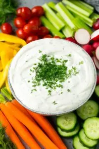 Several veggies including celery, carrots, and tomatoes surrounding a bowl of white veggie dip.