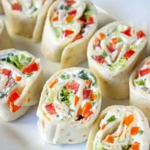 Several veggie pinwheels with peppers, broccoli and onions on a white plate.