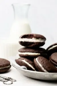 Stack of chocolate whoopie pies with white cream filling on a white plate.