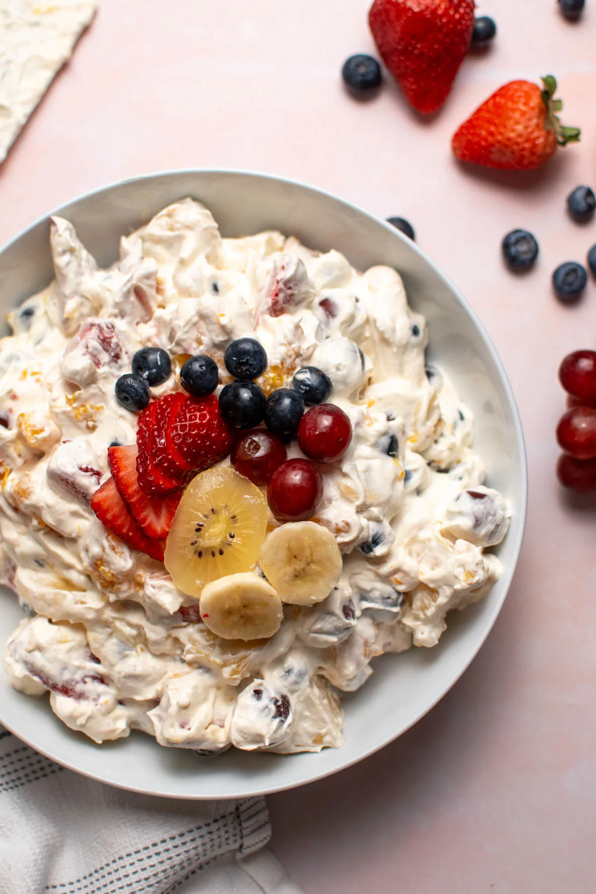 Creamy fruit salad topped with fresh fruit in white bowl.