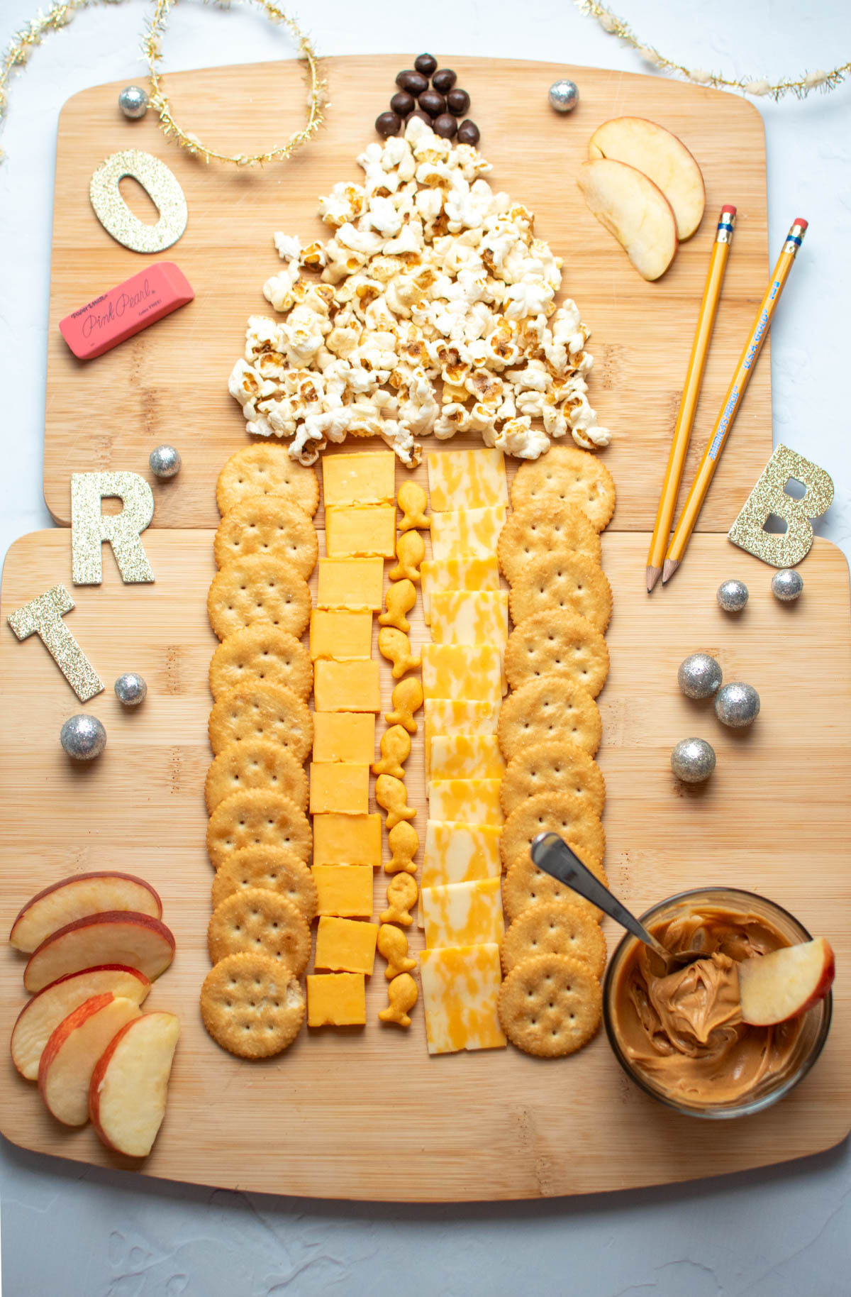 Kids charcuterie board in the shape of a pencil with cheese, crackers, popcorn, and raisins.