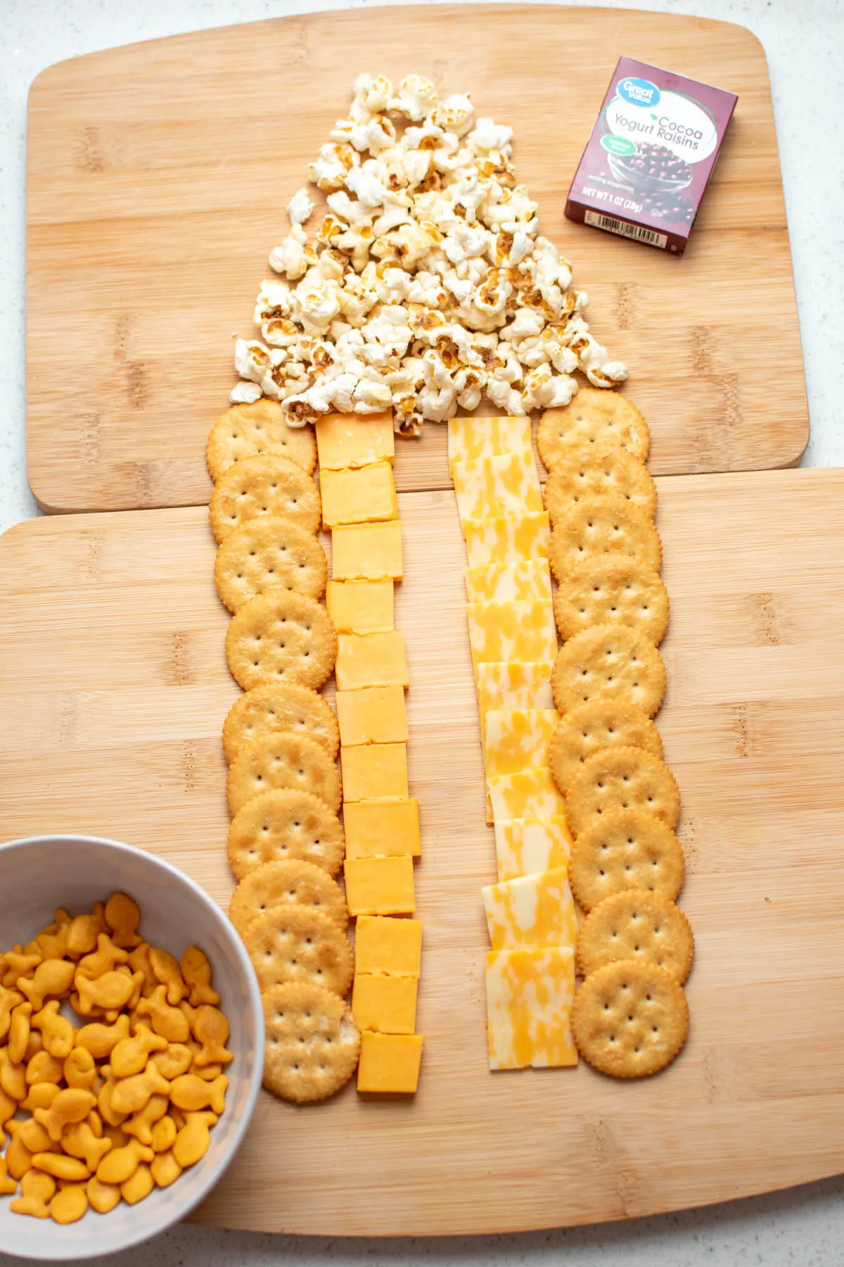 Crackers, cheese, and popcorn on wooden cutting board arranged in a neat pattern.