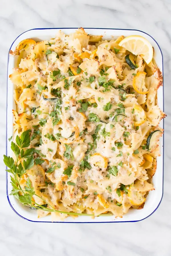 A cheesy chicken casserole with vegetables on a white casserole baking dish.
