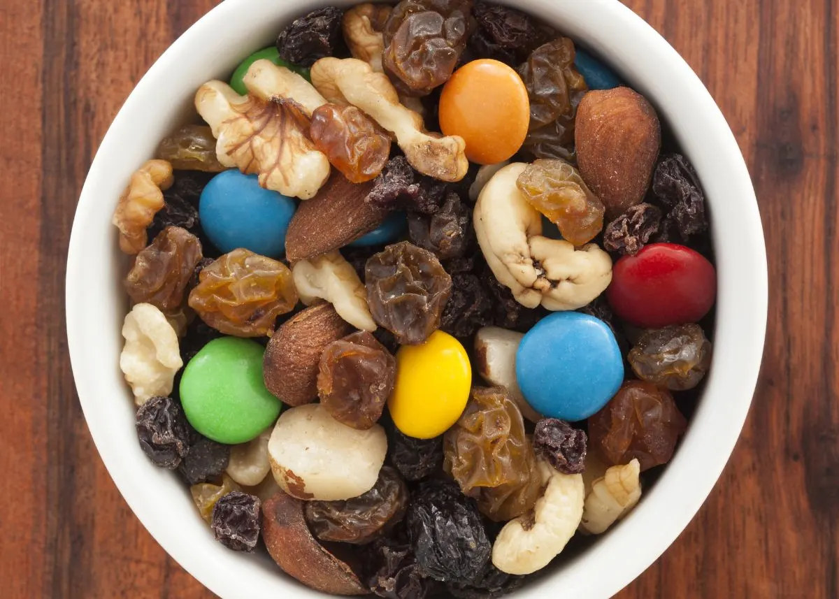 Trail mix in a white bowl with chocolate candies, nuts, and raisins.