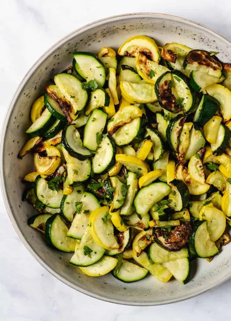 Lighted charred summer squash in a large round serving dish.