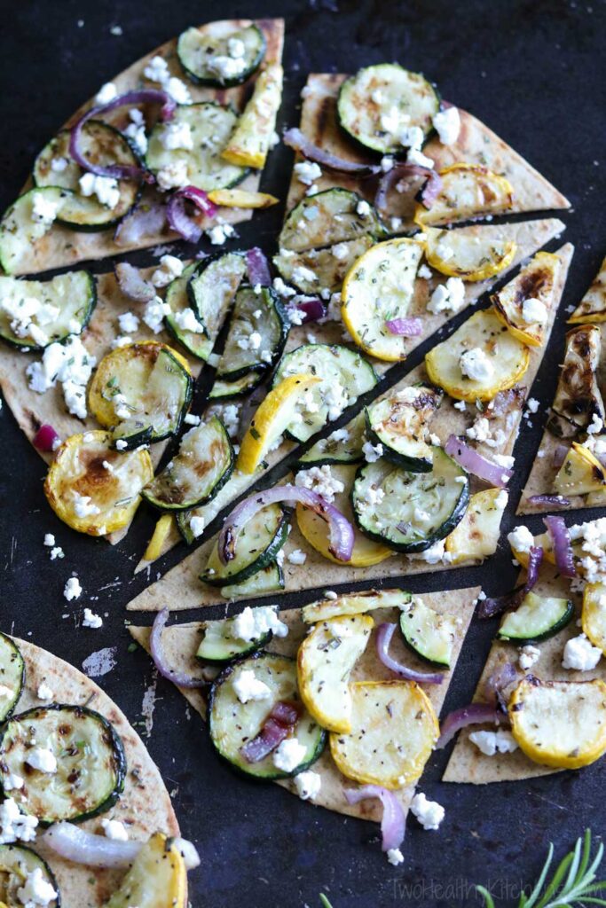 Grilled Flatbread with yellow and green squash on a black background.