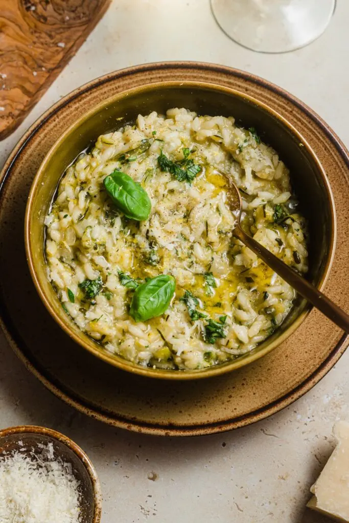 Zucchini risotto with green garnish and olive oil in a brown bowl.