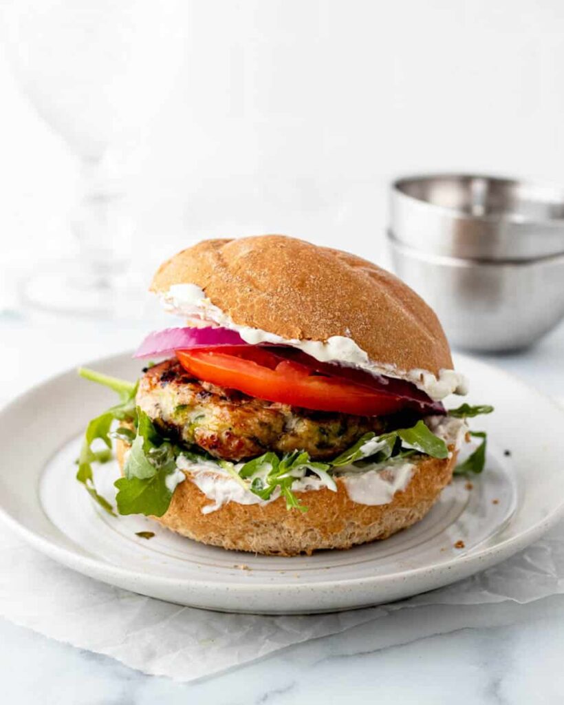 Zucchini turkey burger with tomato on a white plate.