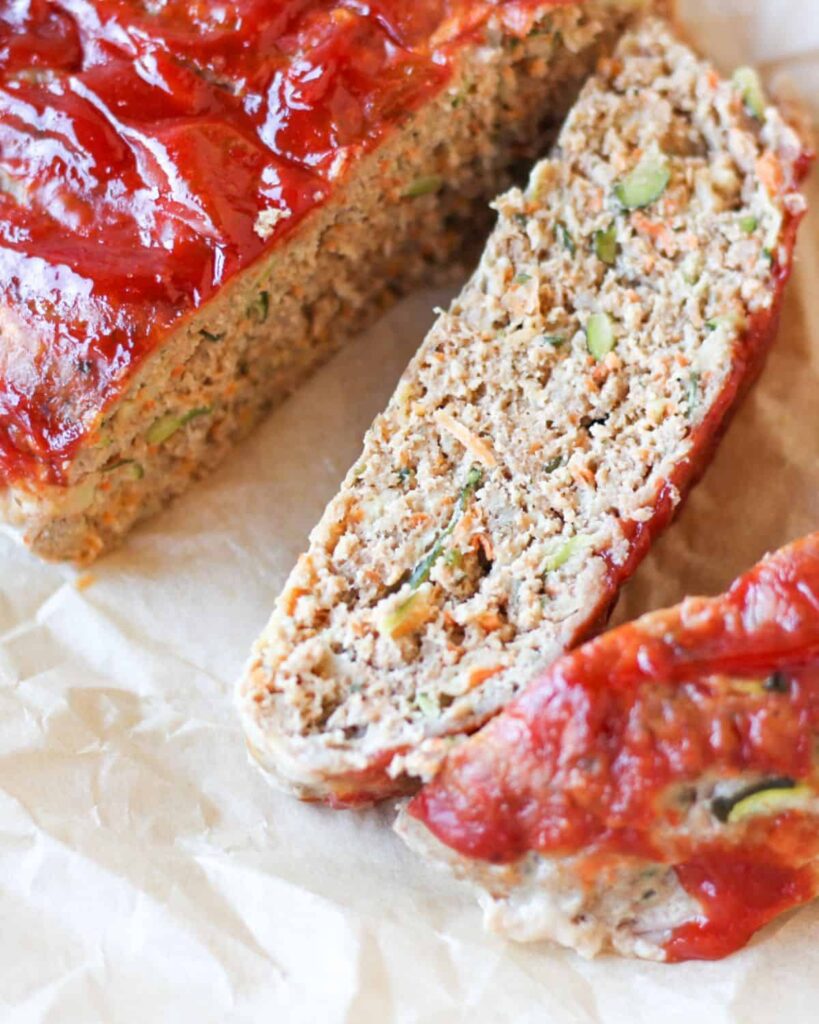 Sliced zucchini meatloaf with red sauce on white parchment paper.