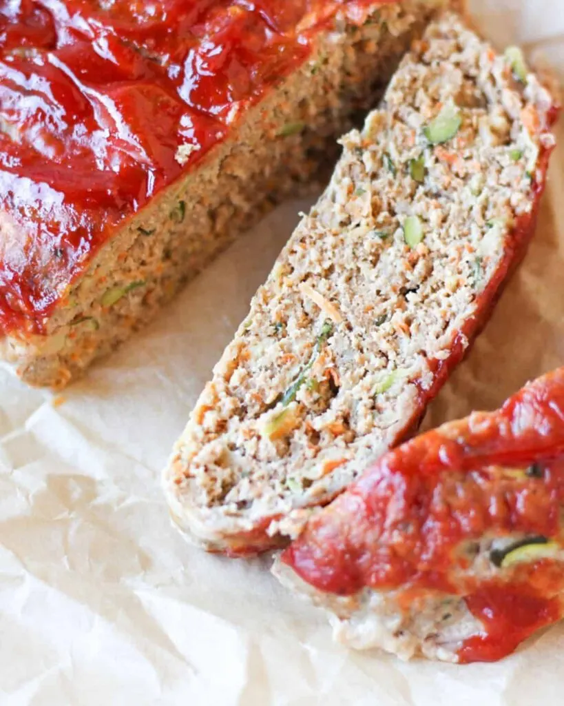 Sliced zucchini meatloaf with red sauce on white parchment paper.