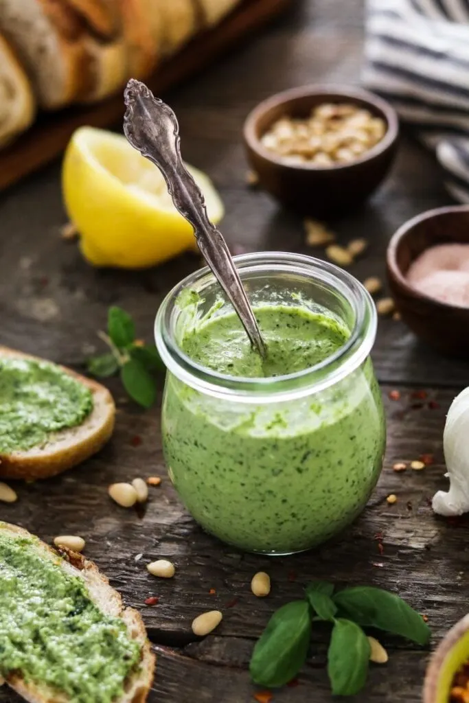 Zucchini pesto in a glass jar with lemon and bread in the background.