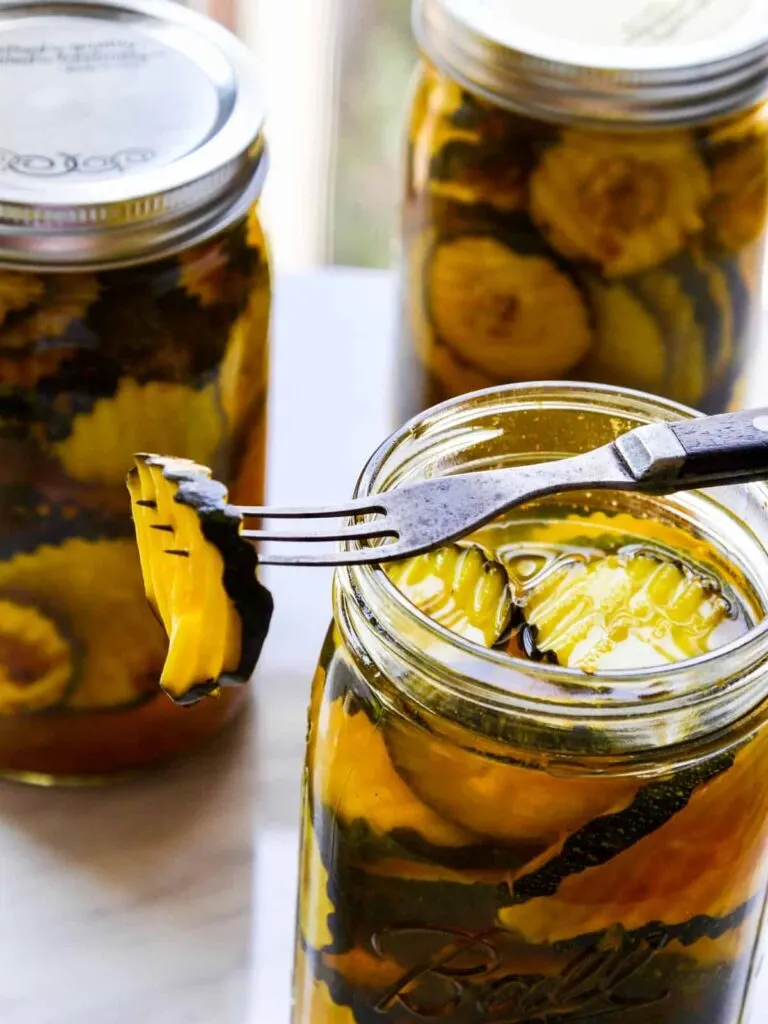 A fork sits on top of a jar of zucchini pickles with a pickle in the tines. 