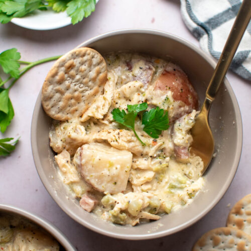 Bowl of creamy chicken stew with fresh parsley, cracker, and spoon in the bowl.