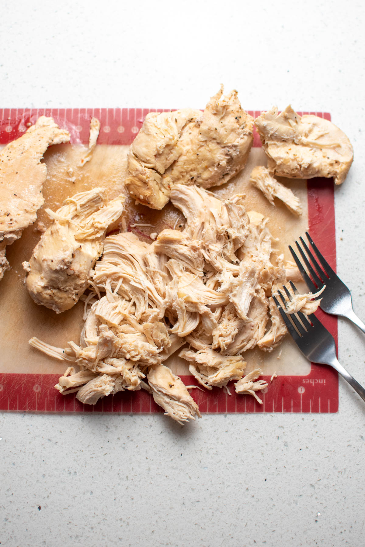 Shredded chicken on cutting board with two metal forks nearby.