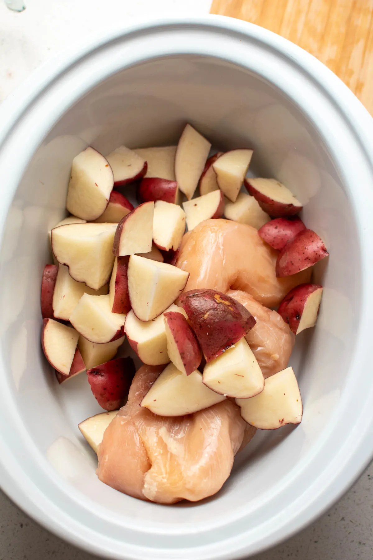 Chopped red potatoes and chicken in white Crockpot insert.