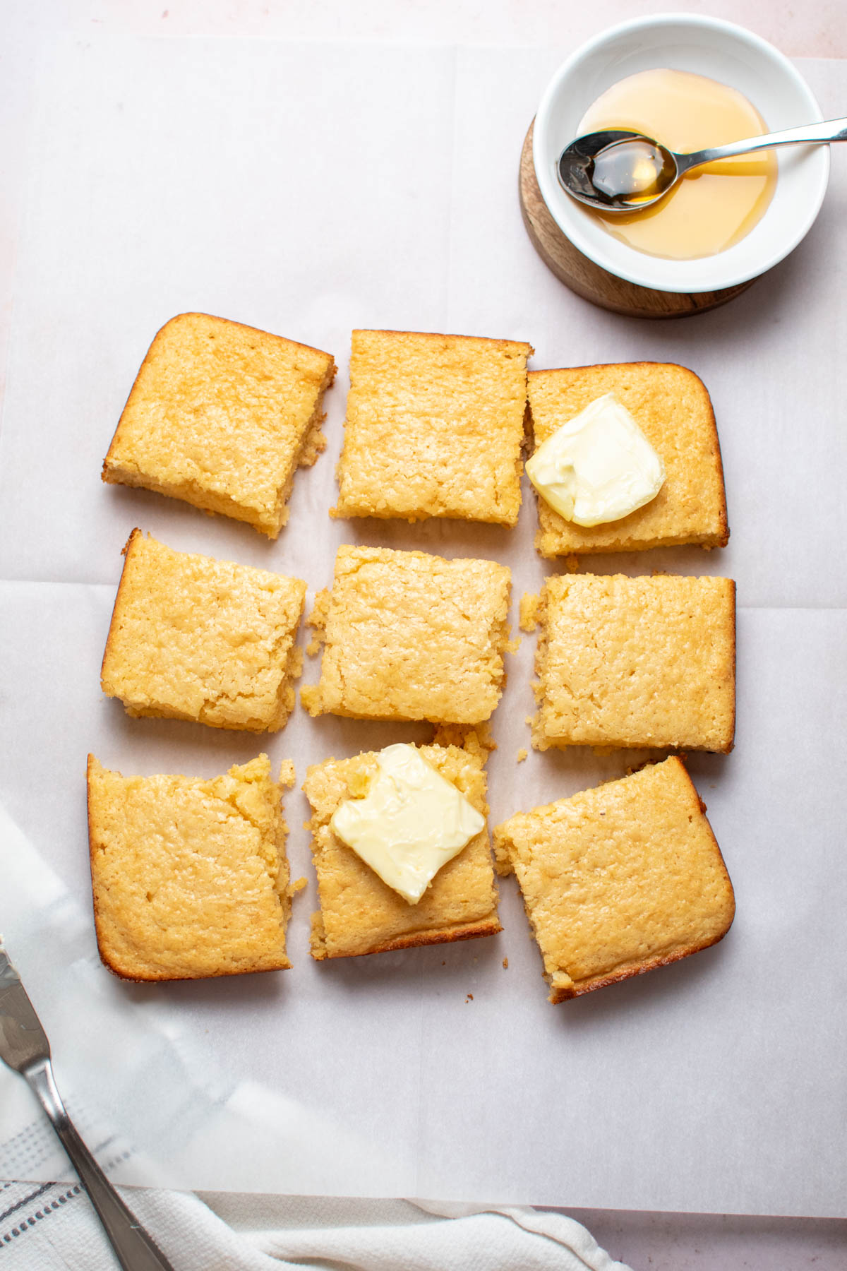 Nine pieces of cornbread arranged on parchment paper with pats of butter on 2 pieces.