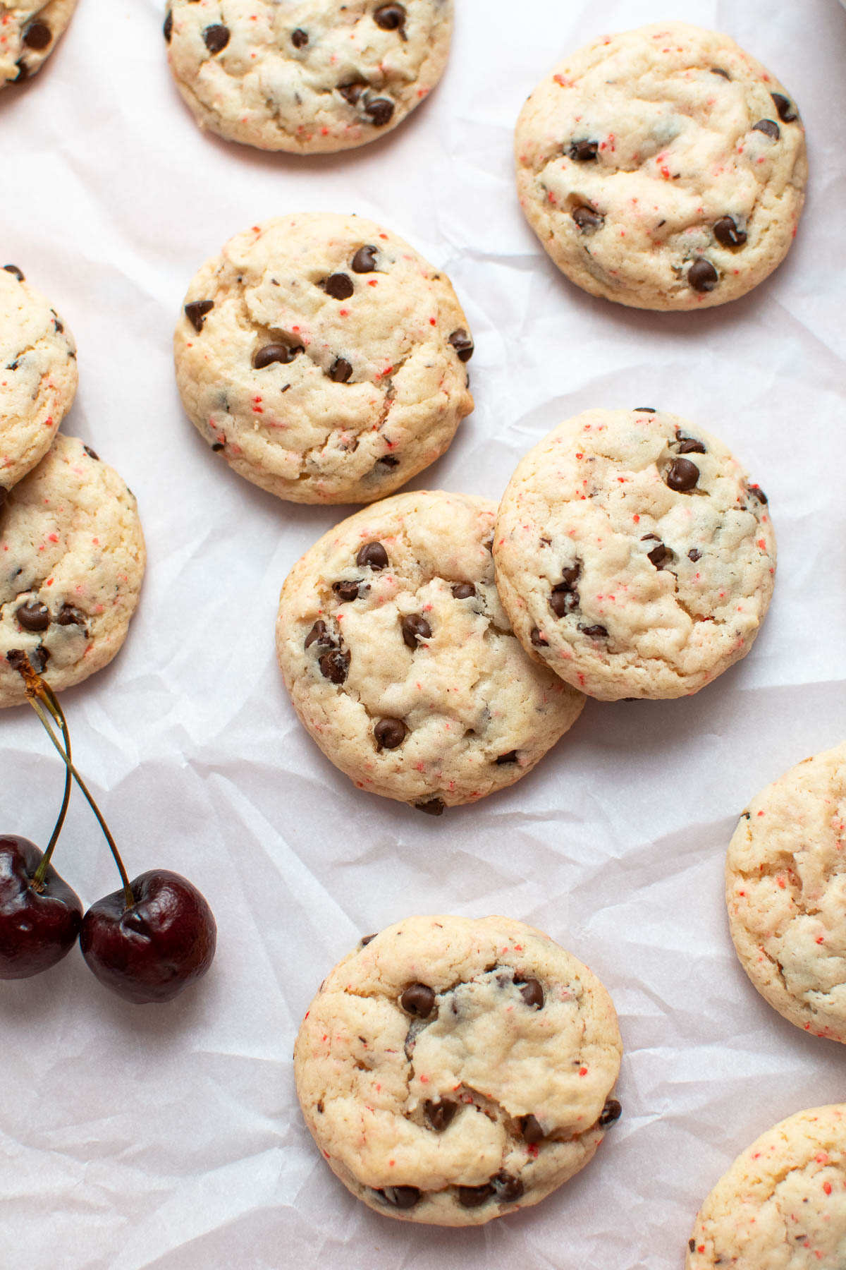 Cherry chip chocolate chip cookies on parchment paper with fresh cherries nearby.