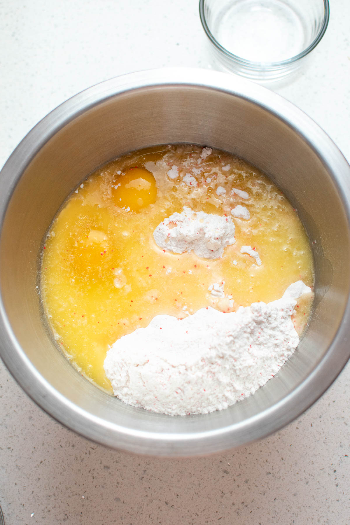Raw eggs, melted butter, and cake mix in metal mixing bowl on quartz countertop.