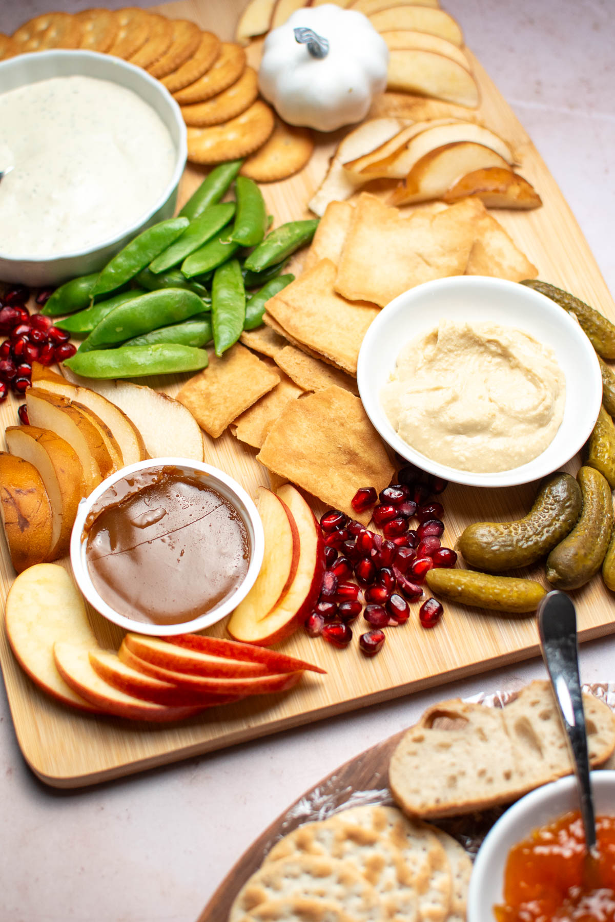 Three bowls of dip and various fruits, vegetables, and crackers on wooden cutting board.