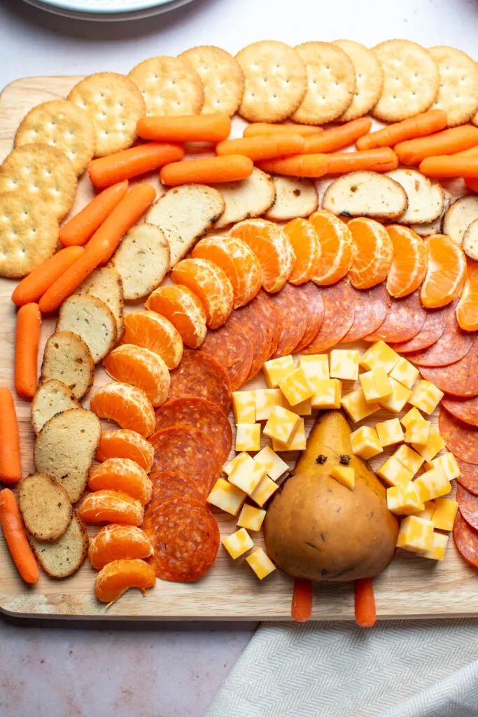 Turkey shaped charcuterie board foods including pepperoni, oranges, and baby carrots.