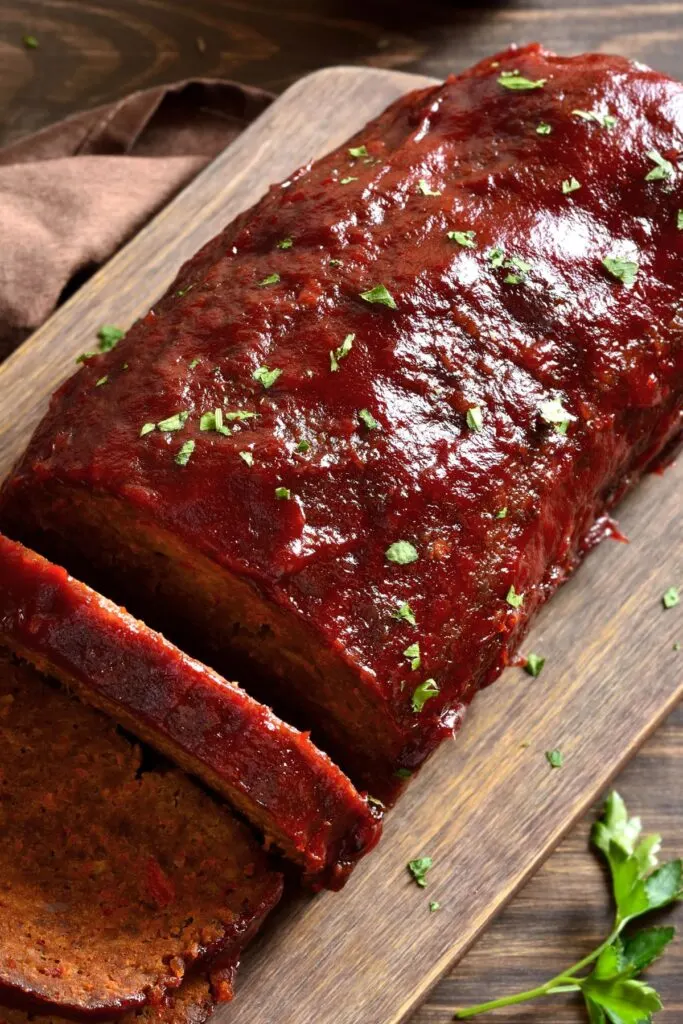 Glazed meatloaf with one slice cut from the loaf on a wooden cutting board.