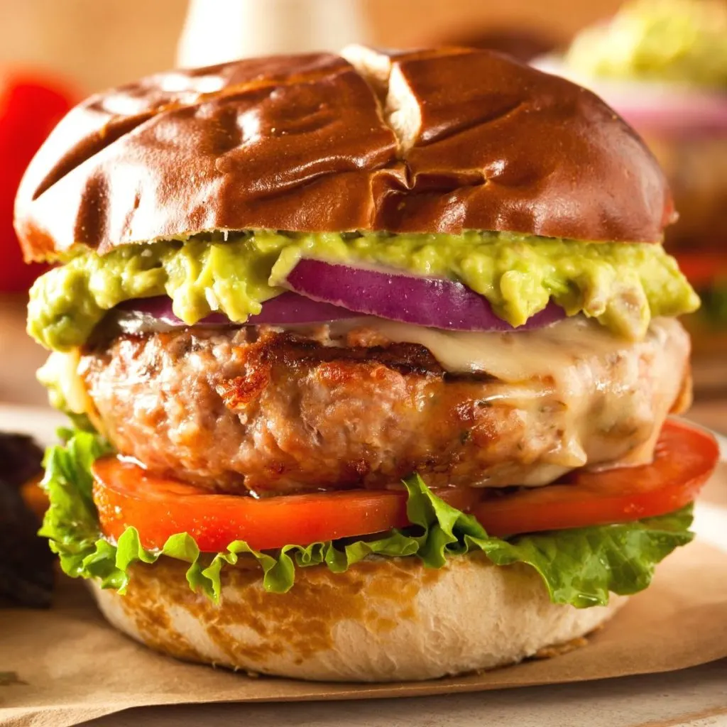 A large burger with a light colored patty, lettuce, red onion, and guacamole.
