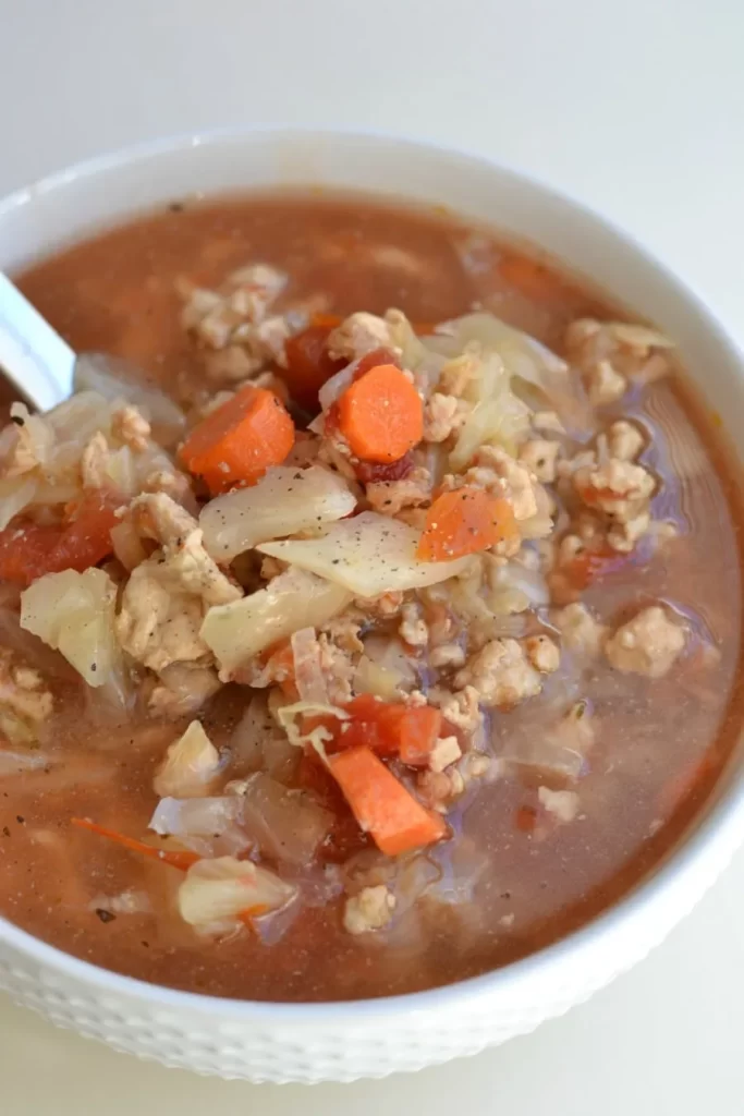 Turkey and cabbage soup with carrots in a large white bowl.