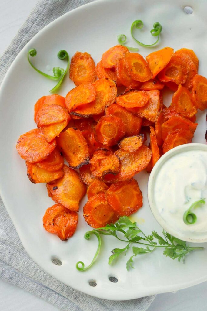 A white plate filled with air fryer carrot chips and a bowl of white dip.