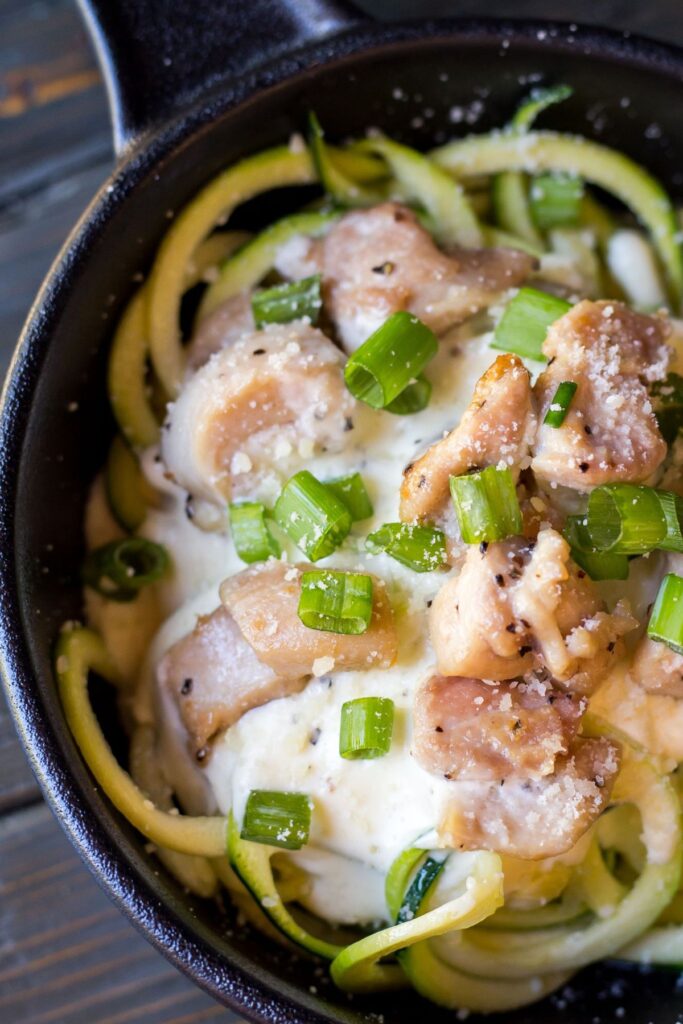 Zucchini noodles with chicken and alfredo sauce in a skillet with green garnish.