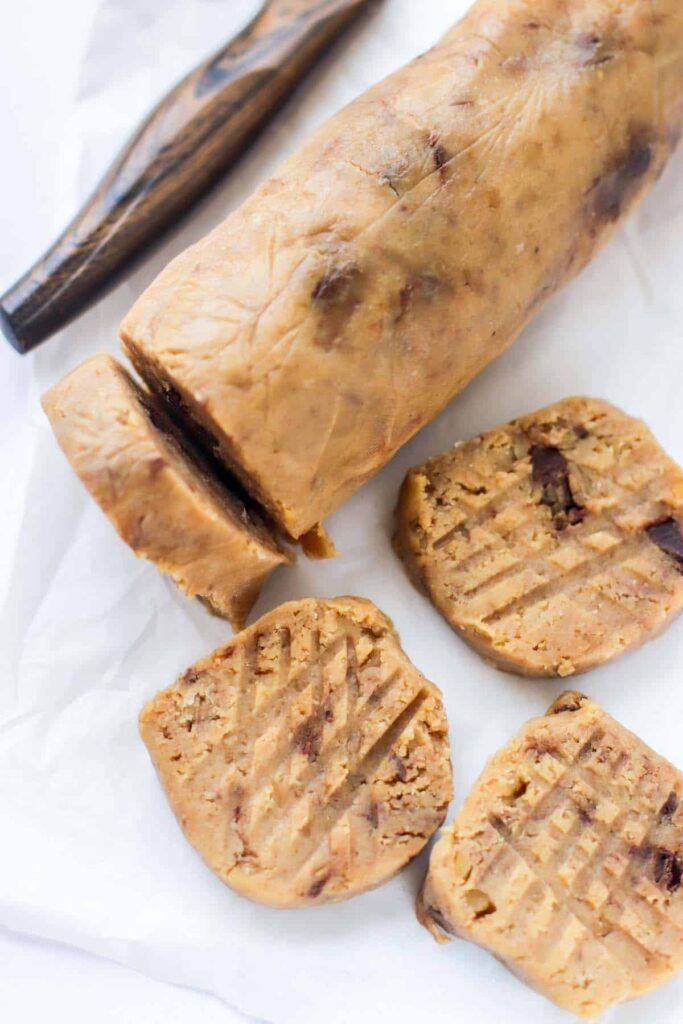 A log of low-cab cookie dough on white parchment paper with a few slices cut off.