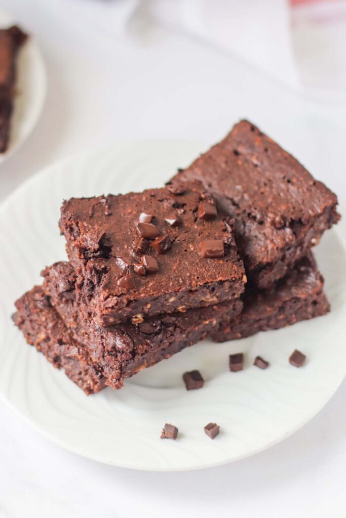 A stack of large and thin brownie squares on a white plate.