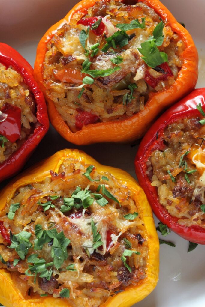 Red and yellow stuffed bell peppers with chicken and cheese on a white platter.