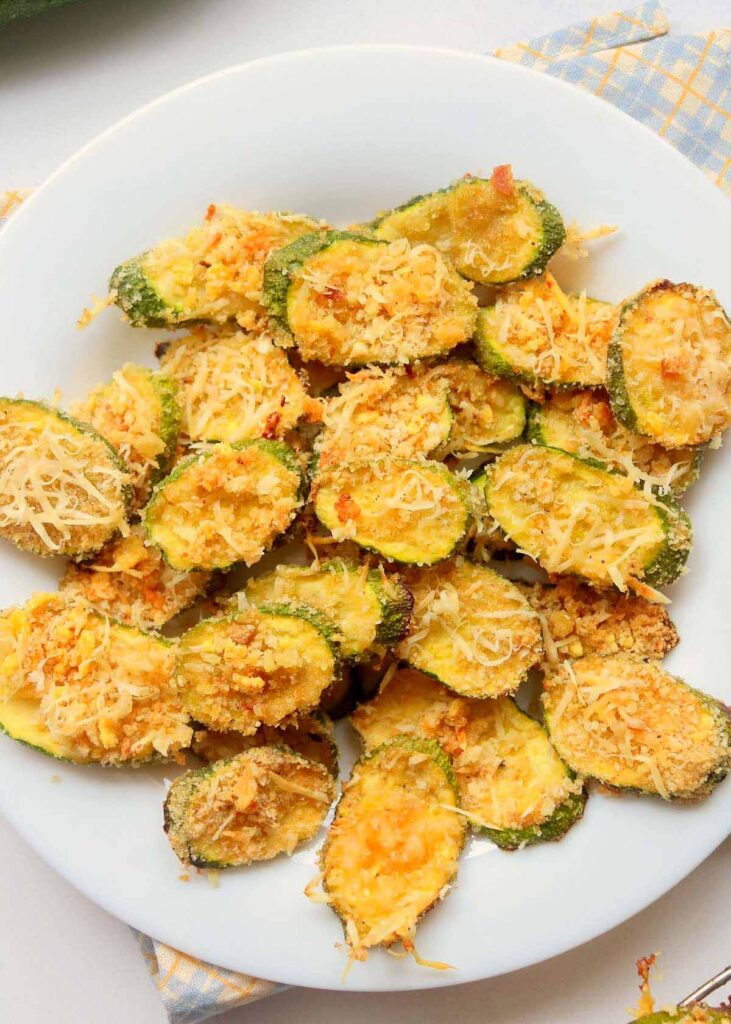 Crispy and cheesy air fryer zucchini chips on a white plate.