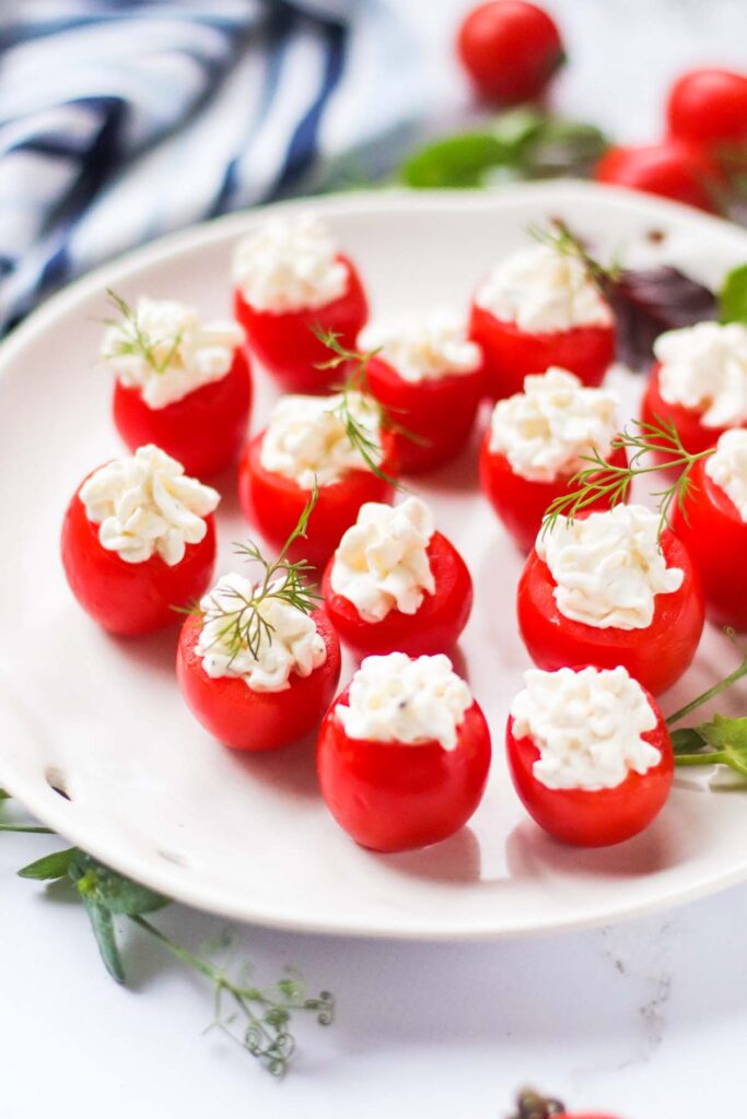 Cherry tomatoes stuffed with white cream on a white serving platter.