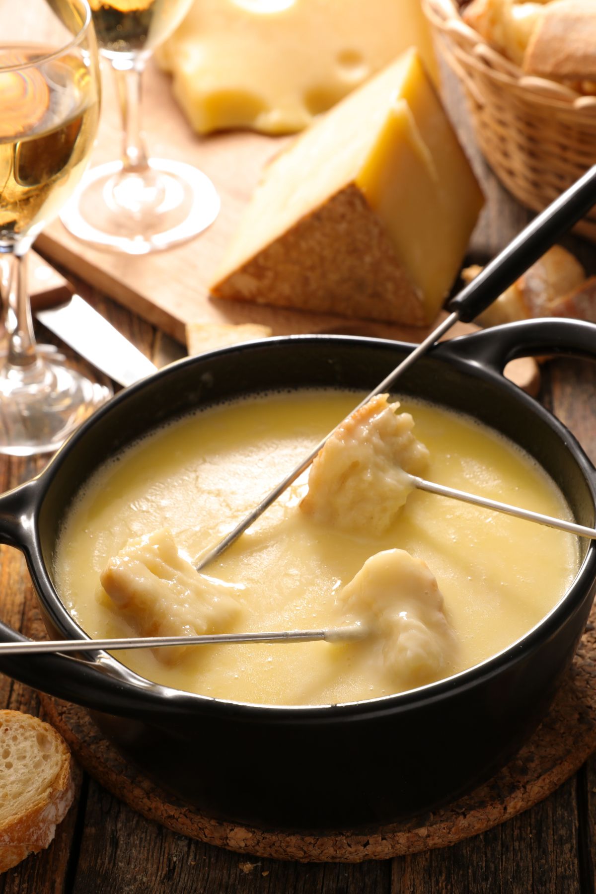 A cheesy fondue pot with bread and sliced cheese in the background.