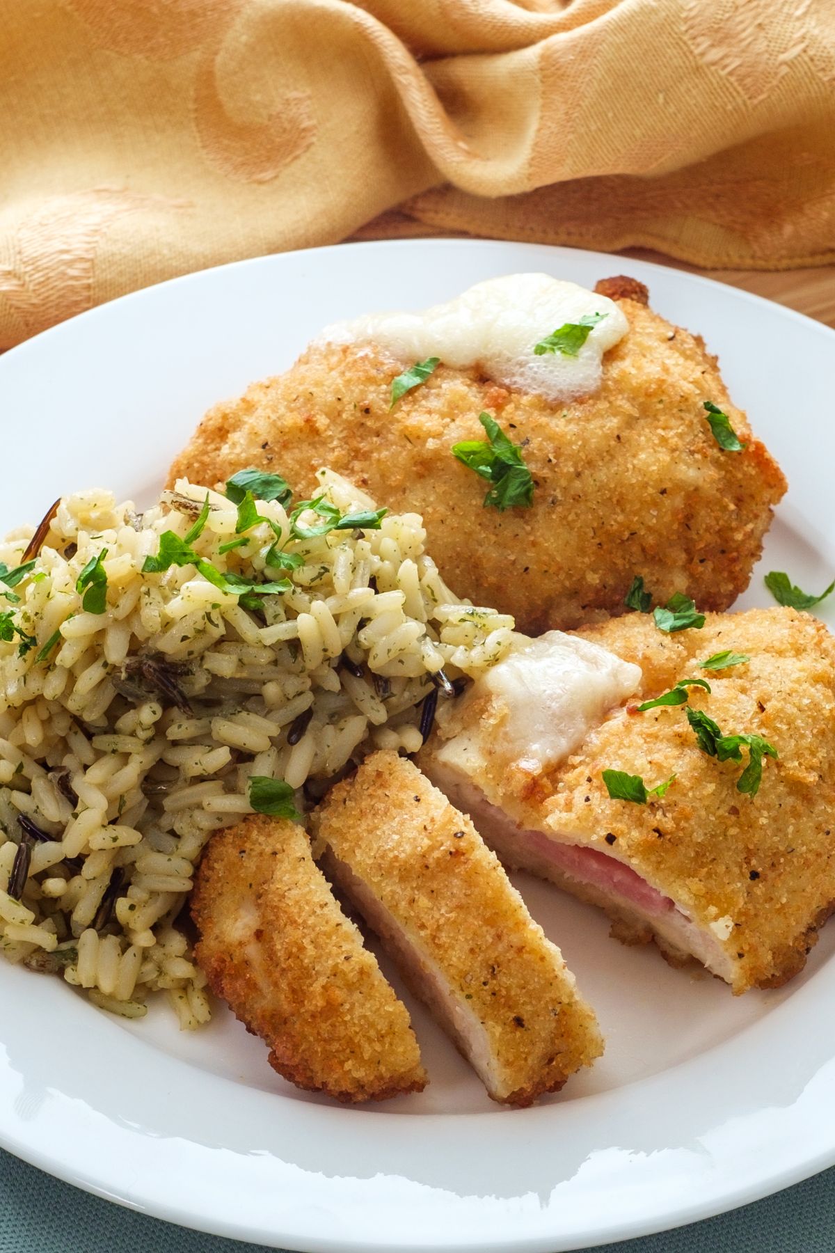 Chicken Cordon Bleu on a white plate with rice and green garnish.