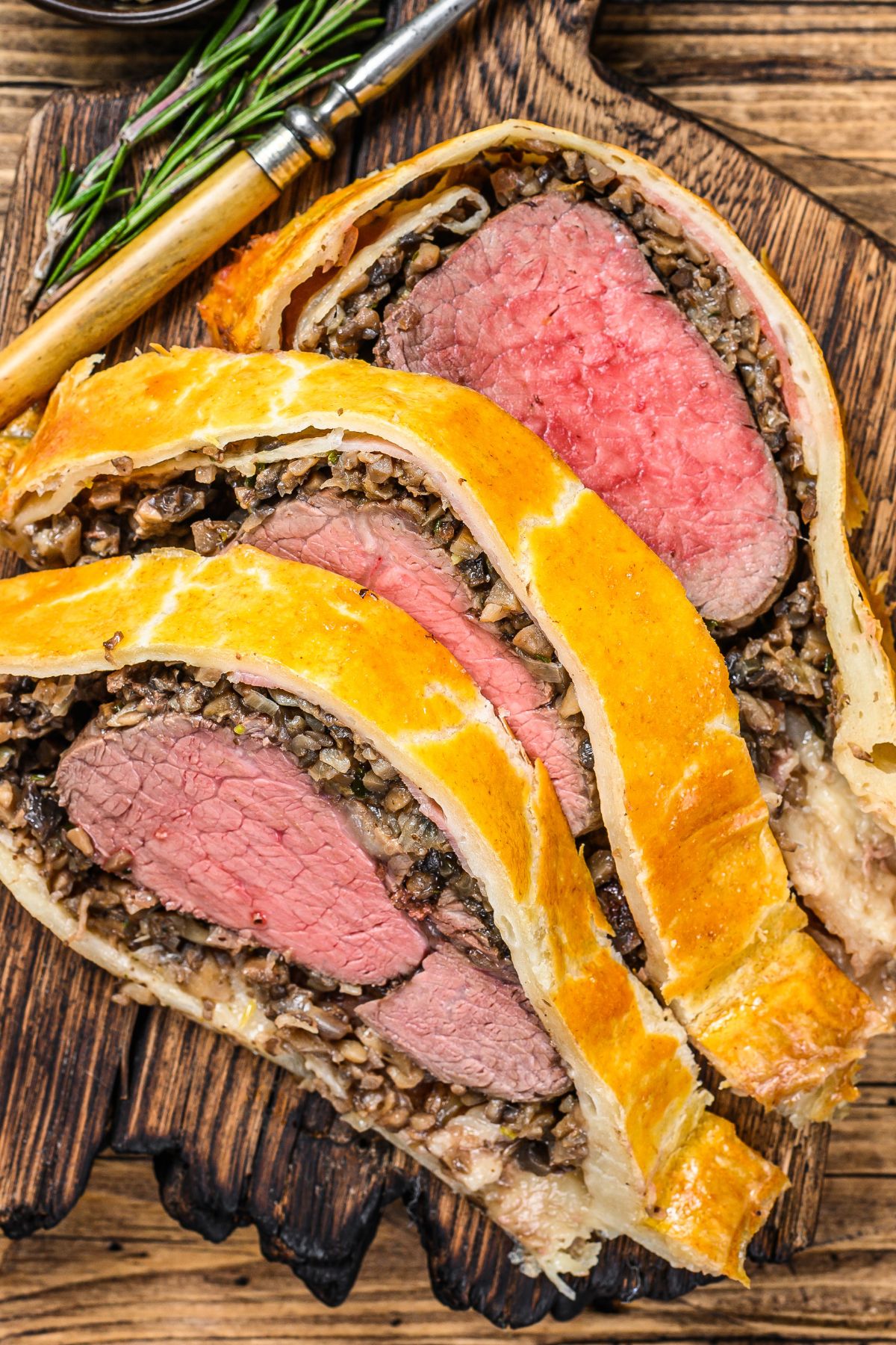 Three thick slices of beef wellington on a wooden cutting board.