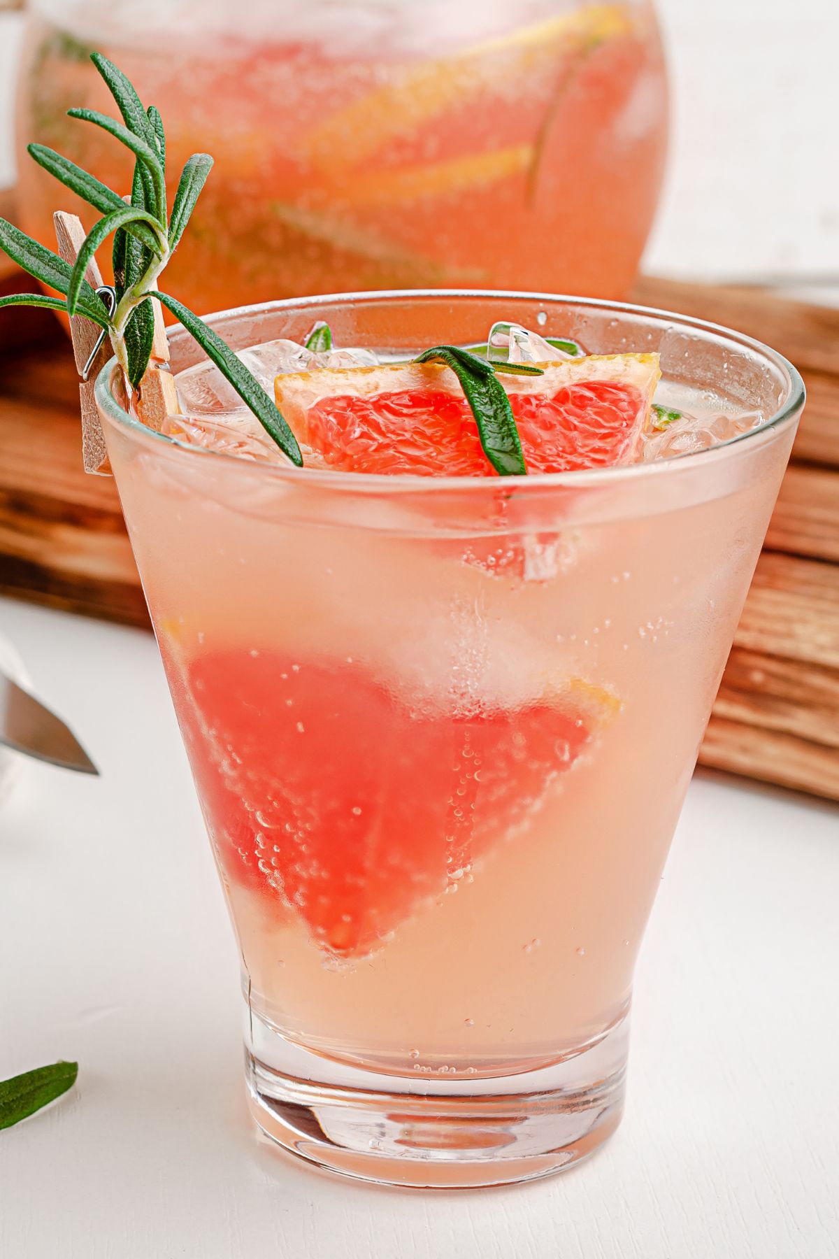 Pink grapefruit mocktail with rosemary garnish in a clear glass.