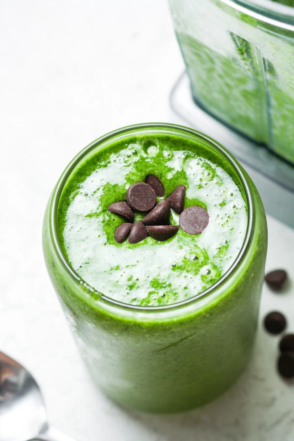 A Green Shake in a clear glass with chocolate chips on top.
