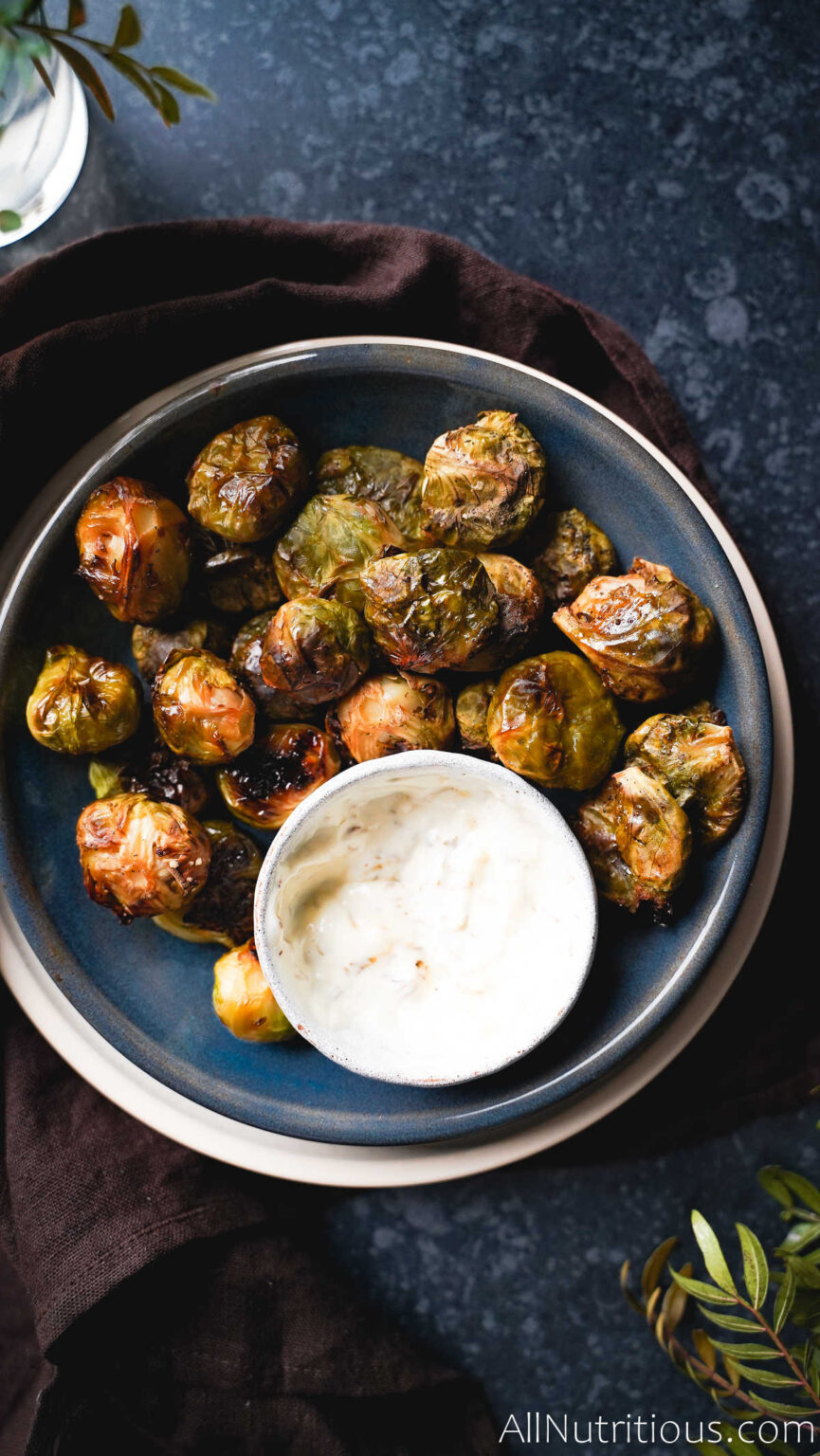 Smashed and roasted Brussels sprouts in a bowl with white dipping sauce.