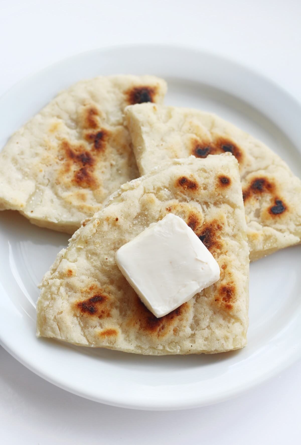 Triangles of Irish potato bread on a white plate with a slice of butter.